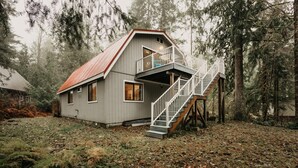 A cabin with a wooden staircase and a balcony, surrounded by dense forest. - 52mbr - Hot Tub - Pets Ok - Generator - Wifi (Deming)