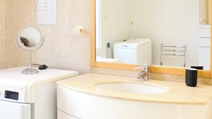 Een badkamer met een wastafel, spiegel en een witte wasmachine.