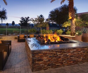 An outdoor fire pit area with seating, surrounded by a brick wall and palm trees. - Luxurious 2/2 Villa at Marriott Shadow Ridge- 'Your Desert Oasis Awaits!' (Palm Desert)