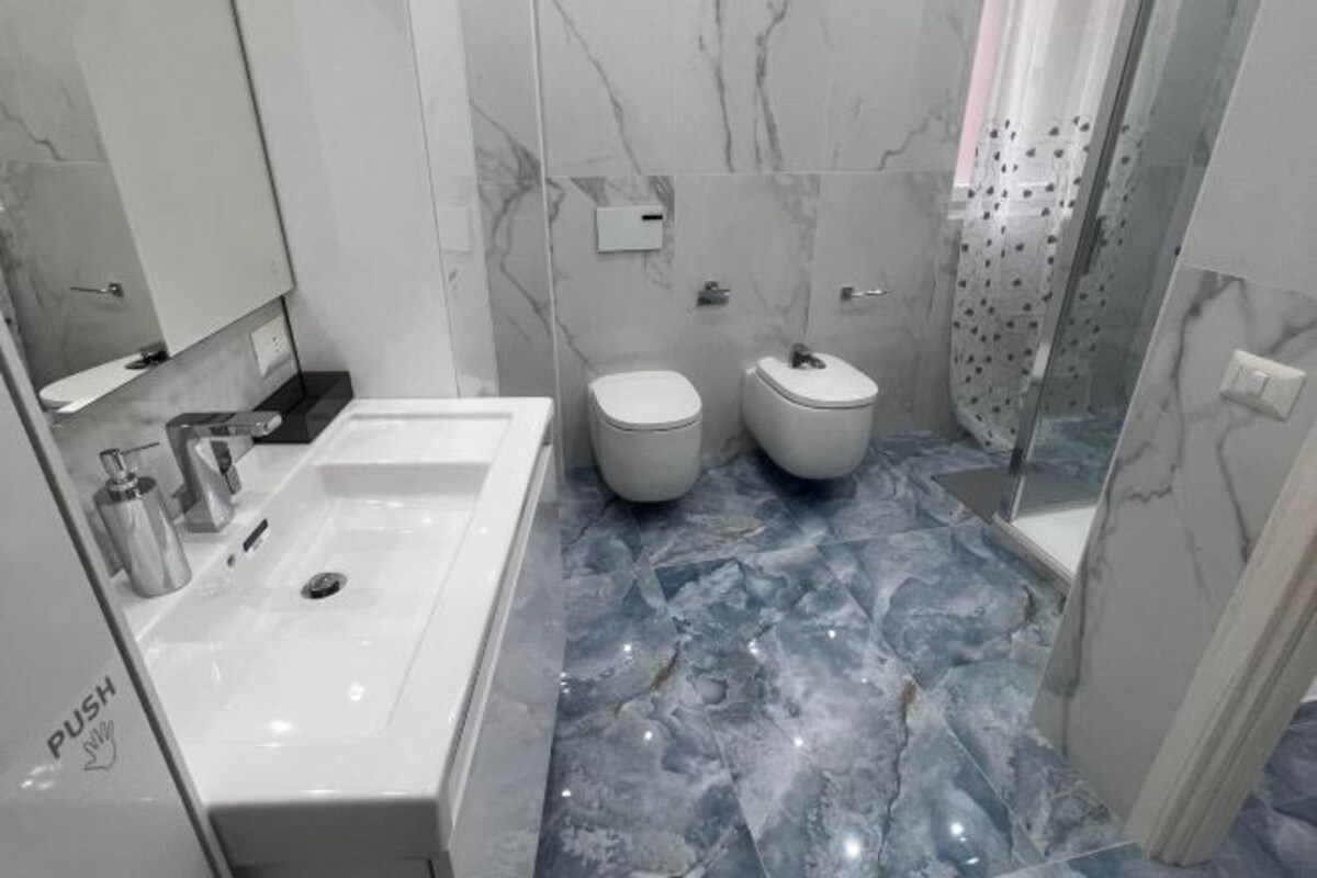 A modern bathroom with a white sink, two toilets, and a shower area.