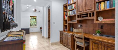 A study room with a wooden desk, bookshelves, a chair, and a window with a view.