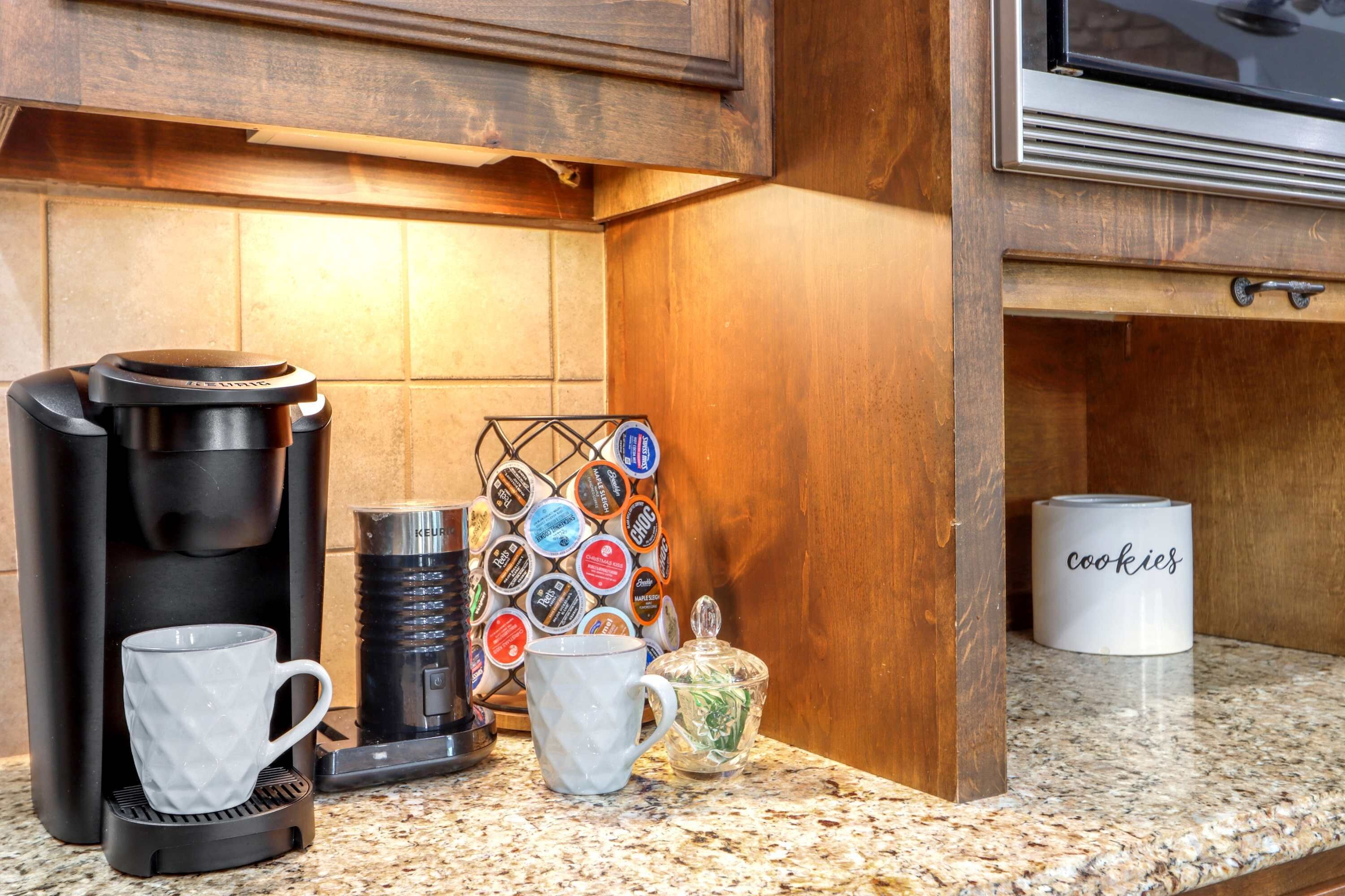 Una encimera de cocina con una cafetera, dos tazas, un portavasos, un tarro y una taza que dice "galletas".