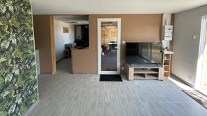 A modern living room with a flat-screen TV, a wooden entertainment unit, and a view into the kitchen area. - Les étoiles du Périgord vert (Gîte ALTAÏR) (Mialet)