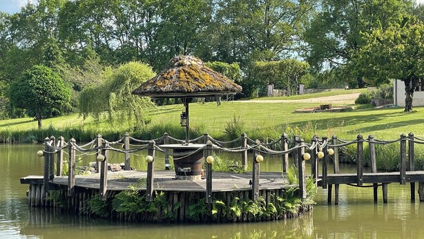 A wooden dock with a thatched-roof gazebo, surrounded by lush greenery and a calm body of water. - Les étoiles du Périgord vert (Gîte ALTAÏR) (Mialet)