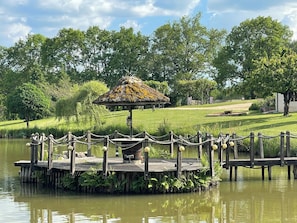 A wooden dock with a thatched-roof gazebo, surrounded by lush greenery and a calm body of water. - Les étoiles du Périgord vert (Gîte ALTAÏR) (Mialet)