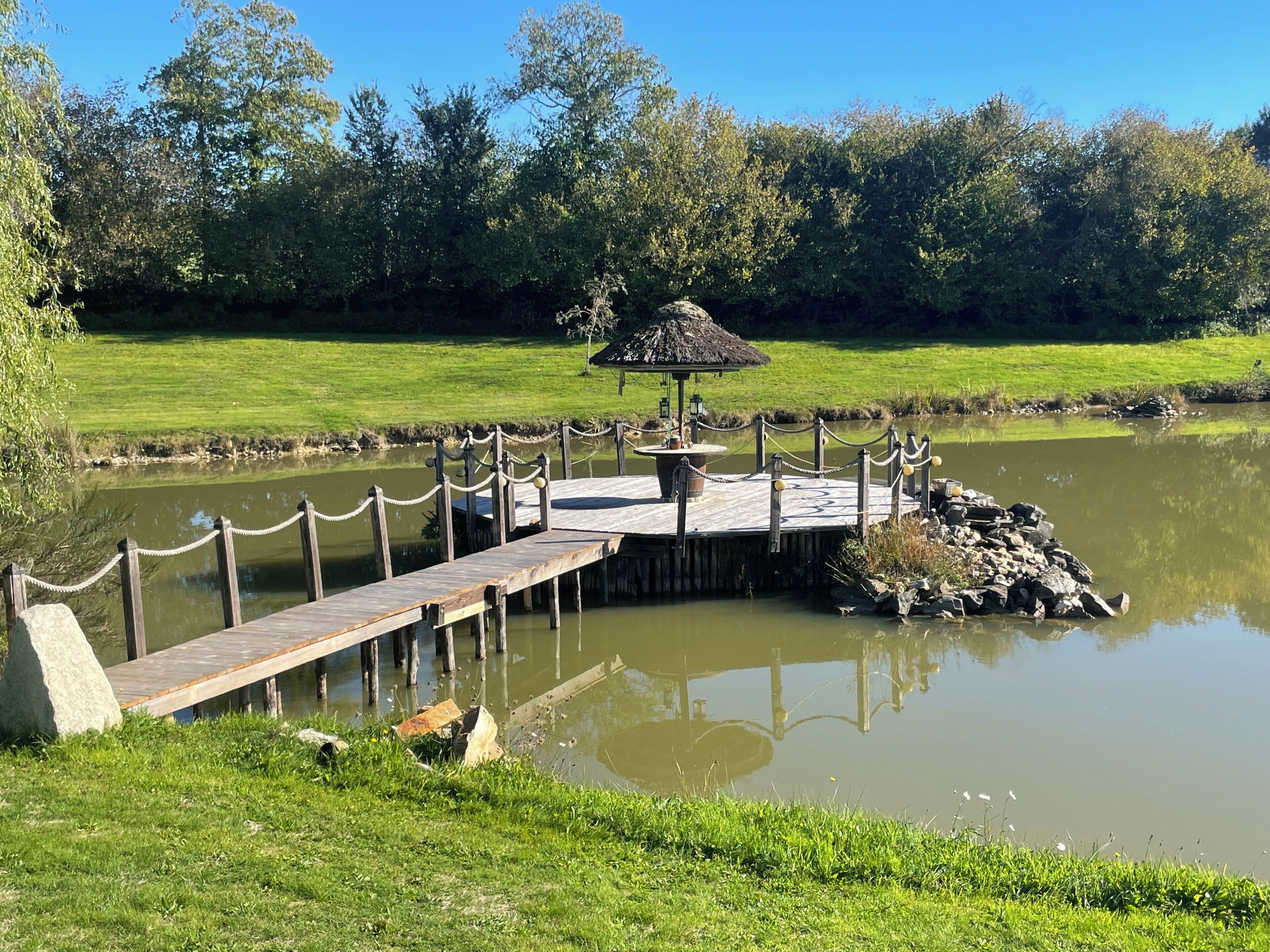 A wooden dock extending over a pond, a gazebo, and a grassy area with trees in the background.