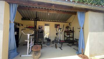Un'area fitness all'aperto, riparata, con attrezzature per esercizi, tra cui una cyclette, un ellittico e pesi.