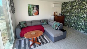A modern living room with a grey sectional sofa, a small round wooden table, a Buddha painting, a clock, and a wall with a leafy pattern. - Les étoiles du Périgord vert (Gîte ALTAÏR) (Mialet)