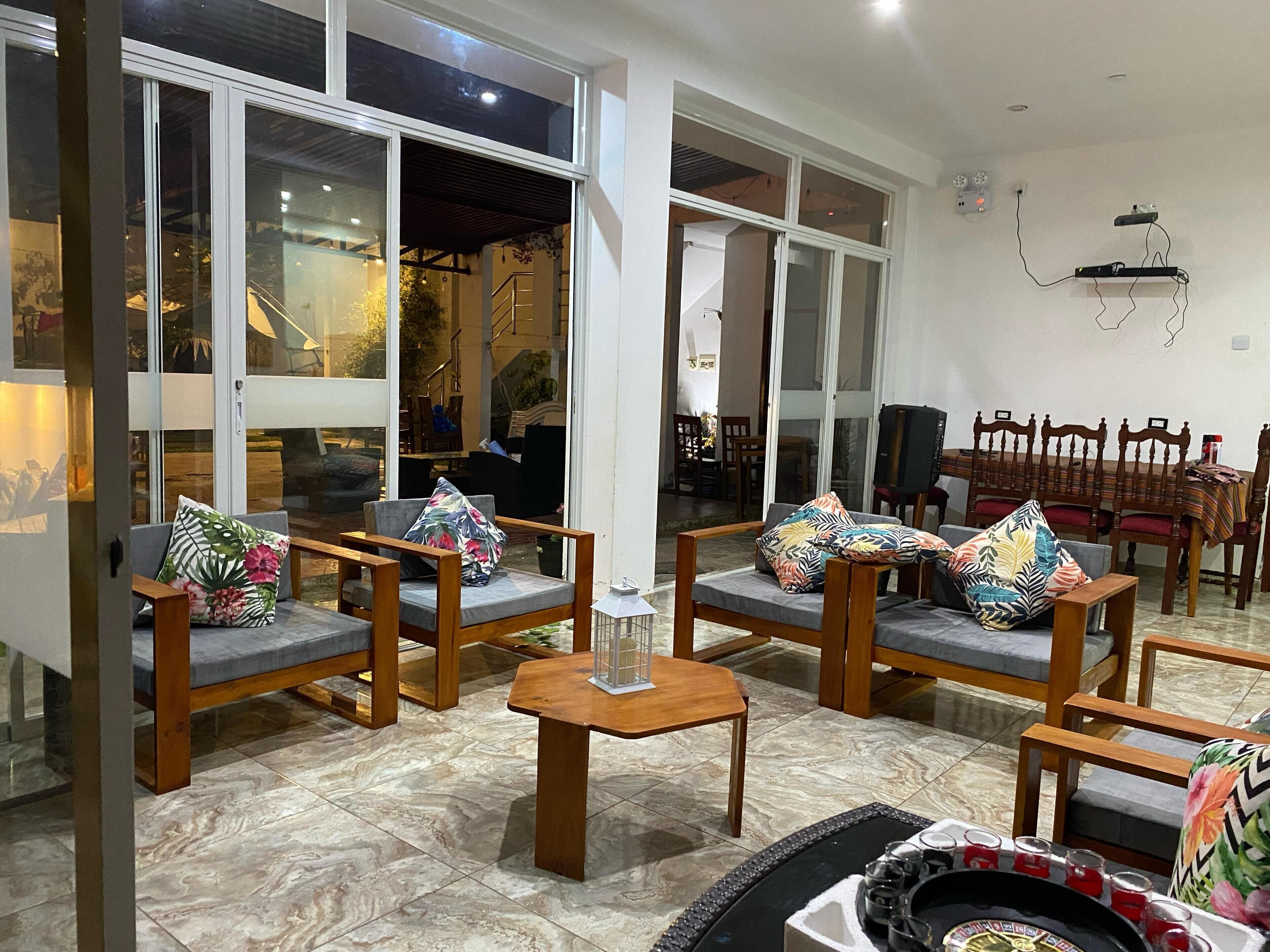 A spacious living area with a high ceiling, large windows, and a dining area with wooden furniture.
