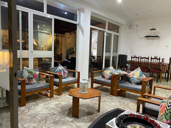A spacious living area with a high ceiling, large windows, and a dining area with wooden furniture.