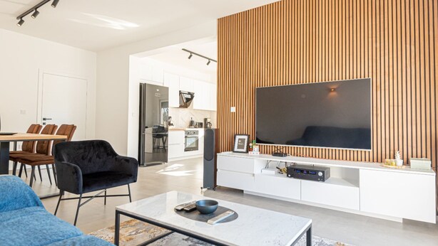 Una sala moderna con un televisor de pantalla plana grande, un sofá, una mesa de centro y una zona de comedor con sillas.