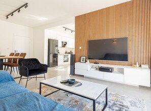 A modern living room with a large flat-screen TV, a sofa, a coffee table, and a dining area with chairs. - Holiday Home Iva (Bilice)