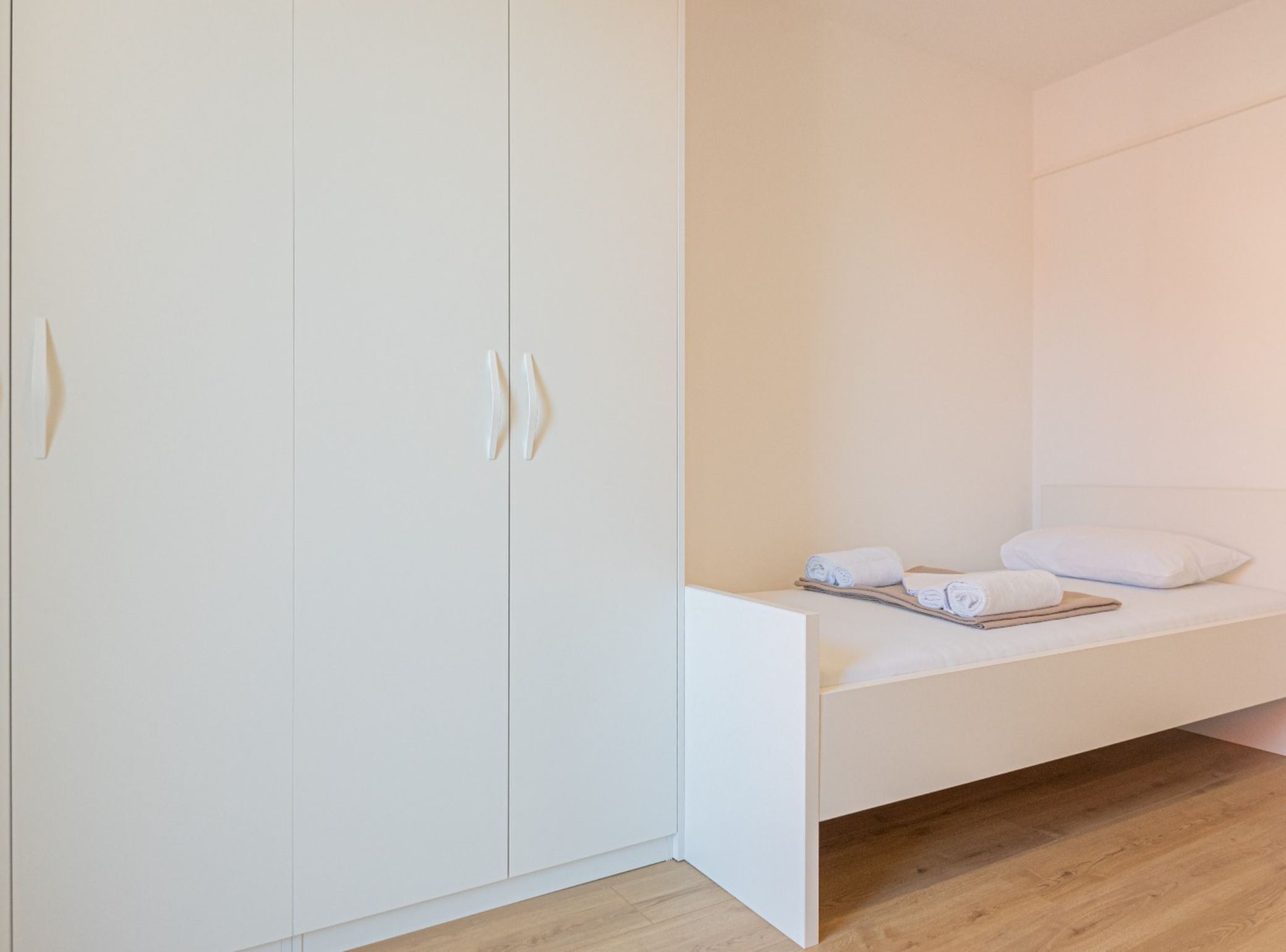 A bedroom with a bed, a wardrobe, and a wooden floor.