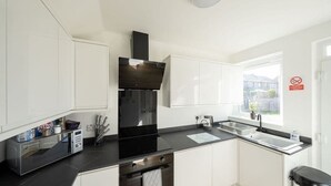 A modern kitchen with white cabinets, a black countertop, a built-in oven, and a window with a view. - Derry House - spacious 3 bed house with driveway (Aberdeen)