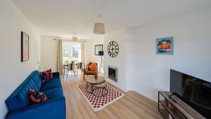 A modern living room with a blue sofa, a TV, a fireplace, and a dining area in the background. - Derry House - spacious 3 bed house with driveway (Aberdeen)