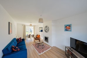Una sala moderna con un sofá azul, un televisor, una chimenea y un comedor al fondo.
