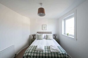 Un dormitorio con cama, lámparas de noche, una ventana y una lámpara colgante.