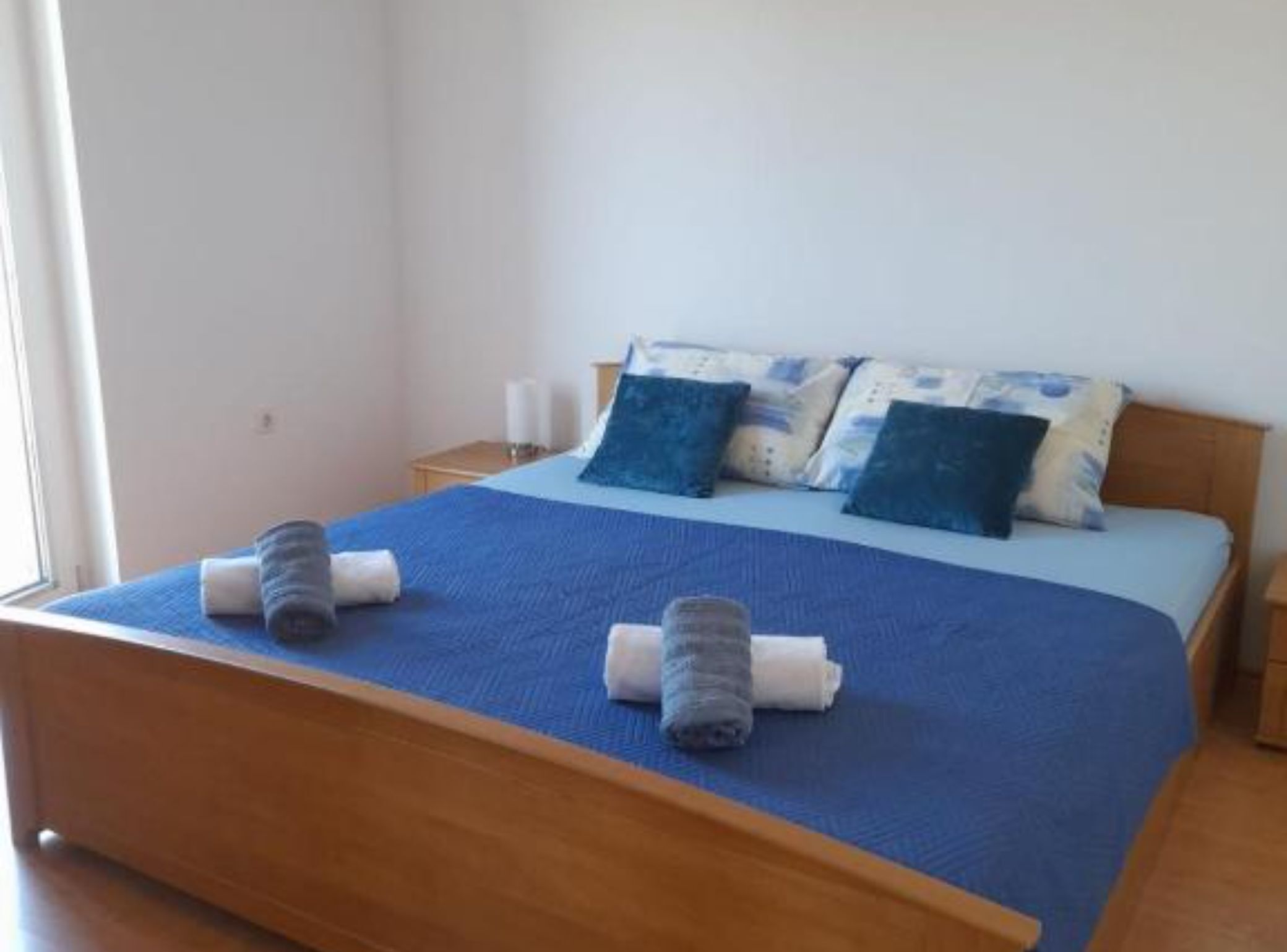 A neatly made bed with blue bedding and pillows, a wooden headboard, and a small bedside table with a lamp.