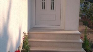 A white door with a small window, a set of steps leading up to it, and potted plants on the ground. - Villa Anita (Unesic)