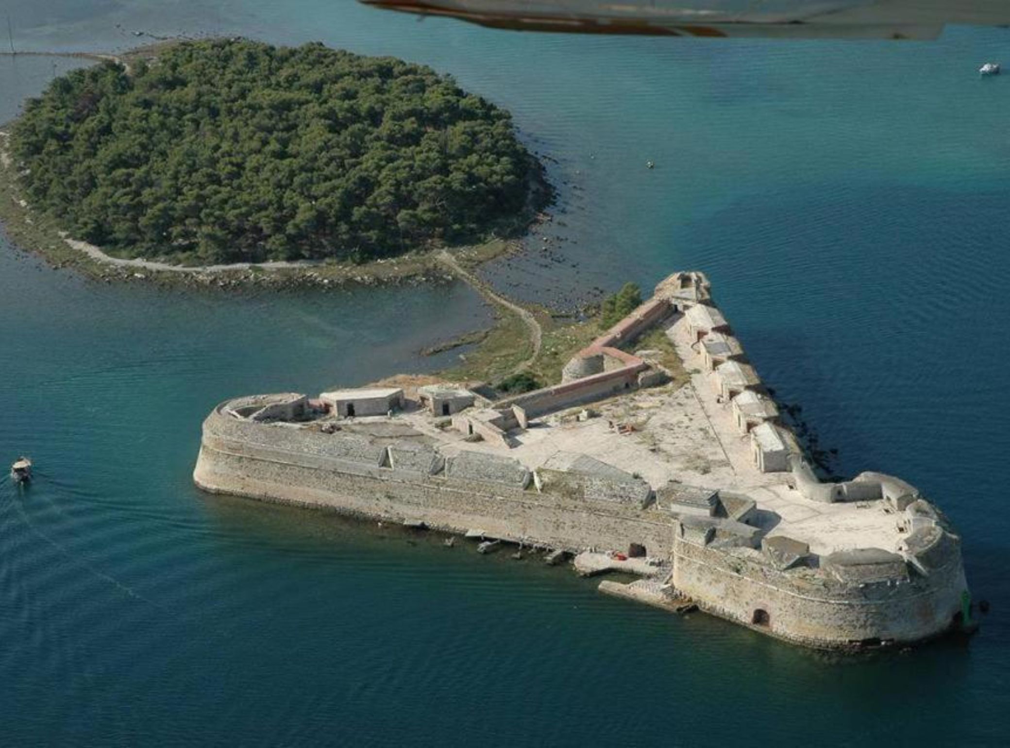 An aerial view of a fortified island with a central fortress and a smaller island nearby.