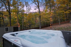 A hot tub surrounded by trees with autumn leaves, set in a backyard with a wooden deck and a small shed.