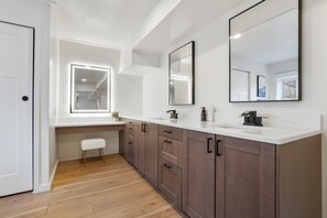 Un baño moderno con un espejo grande, un tocador con lavamanos y una ventana que proporciona luz natural.