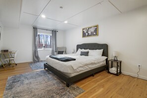 A modern bedroom with a large bed, a desk, and a window with curtains.