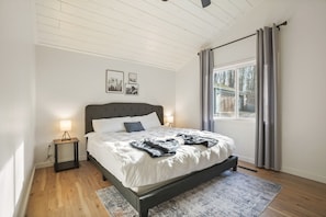 Un dormitorio con cama, mesitas de noche, una ventana con cortinas y vistas al exterior.