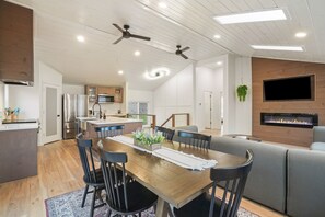 A modern kitchen with a dining area, a built-in fireplace, and a TV mounted on the wall. - The Haven @ Hocking | Luxury Retreat, Hot Tub (Rockbridge)