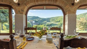 A dining table set with wine glasses, plates, and a vase of flowers, with a view of a mountainous landscape through large windows. - Private villa with pool, hot tub and garden in the Tuscan countryside (Castel Focognano)