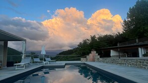 A swimming pool with lounge chairs and umbrellas, surrounded by stone walls and a view of the sky with clouds. - Private villa with pool, hot tub and garden in the Tuscan countryside (Castel Focognano)