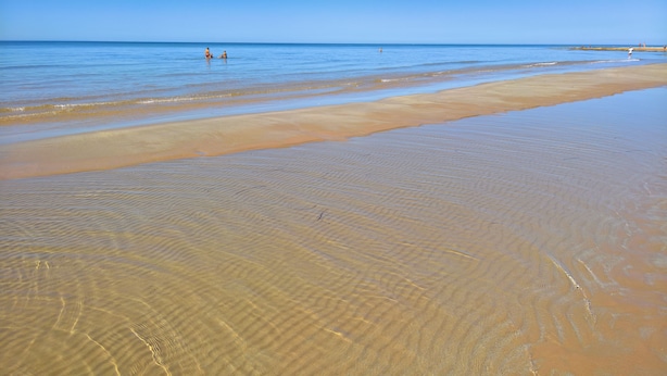 A beach with clear shallow waters and a sandy shore.