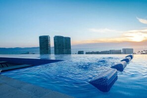 Une piscine à débordement offrant une vue sur deux bâtiments modernes et un coucher de soleil.