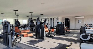 Een fitnessruimte met diverse trainingsapparaten, waaronder gewichtbanken en cardioapparatuur.