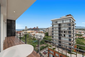 Un balcon offrant une vue sur le paysage urbain, avec des bâtiments modernes et une étendue d’eau.