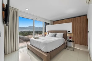 Une chambre d’hôtel moderne avec un grand lit, une table de chevet, une télévision et une vue sur les montagnes.