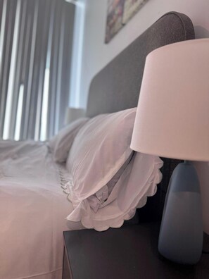 A neatly made bed with white bedding and a decorative pillow. A modern lamp with a white shade is placed on a dark nightstand beside the bed. - City Centre - 2-bed High Rise Apartment - Sleeps 4 (Manchester)