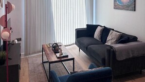 A modern living room with a dark sofa, a coffee table, and a blue armchair. - City Centre - 2-bed High Rise Apartment - Sleeps 4 (Manchester)