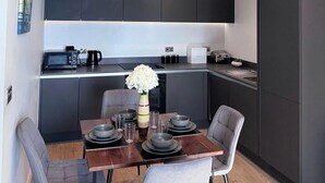 A modern kitchen with dark cabinets, a dining table set with plates and glasses, and a vase of flowers. - City Centre - 2-bed High Rise Apartment - Sleeps 4 (Manchester)