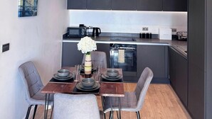 A modern kitchen with dark cabinets, a dining table set with plates and glasses, and a vase of flowers. - City Centre - 2-bed High Rise Apartment - Sleeps 4 (Manchester)
