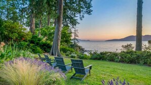 Un jardin paisible offrant une vue sur l’eau, agrémenté de chaises vertes et d’une végétation luxuriante.