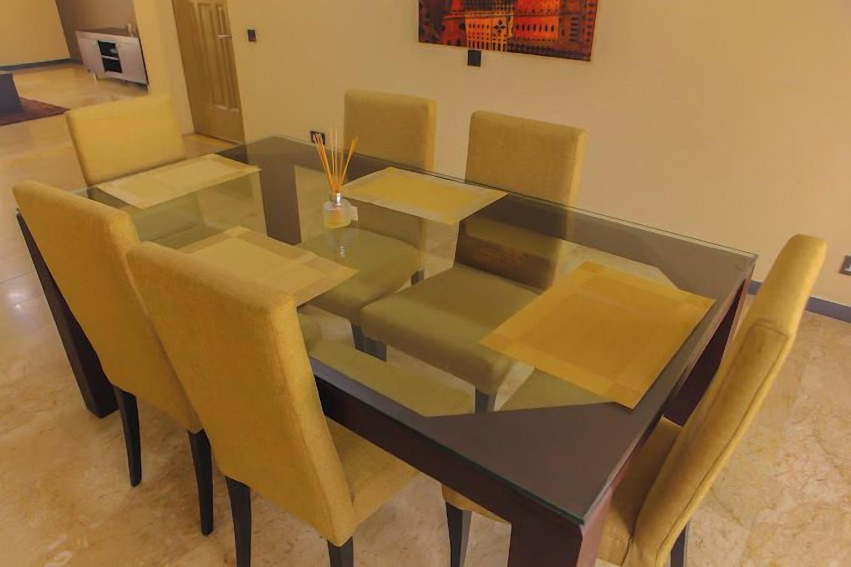 Un comedor con una mesa de vidrio rodeada de sillas tapizadas en color amarillo.