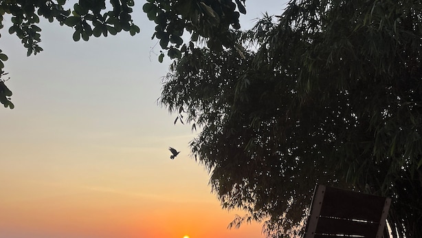 Eine Holzterrasse mit Liegestuhl und Blick auf den Sonnenuntergang über dem Meer.