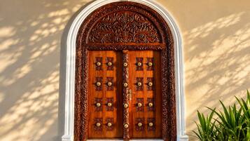 A double wooden door with intricate carvings and a white archway.