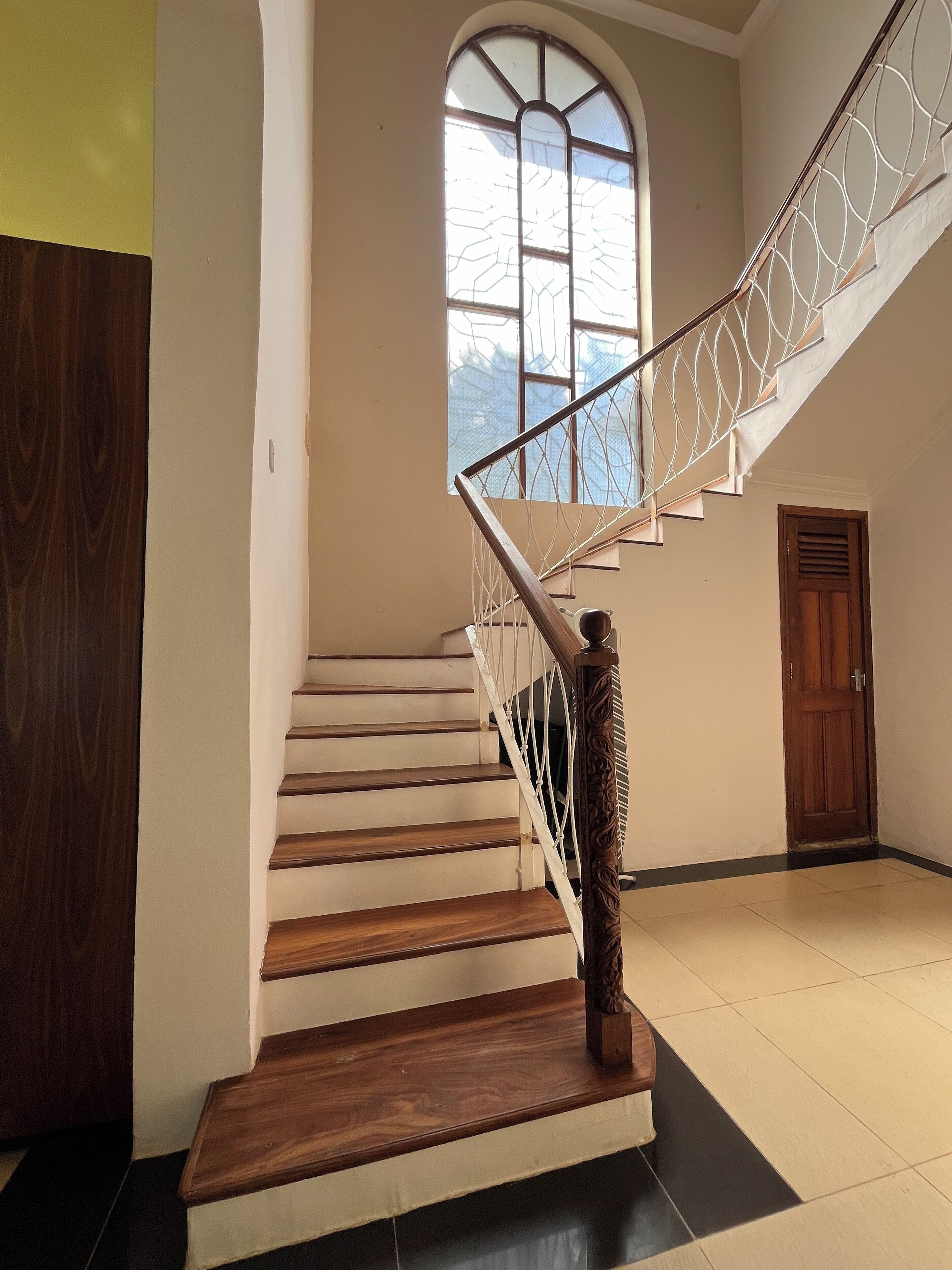 Un escalier avec des marches en bois et une rampe décorative, menant à un palier doté d’une grande fenêtre en arc de cercle.
