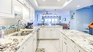 A kitchen with white cabinets, granite countertops, and a central island. - Tropical & Elegantly Updated Oceanfront Townhome (Key Colony Beach)
