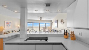 A modern kitchen with a large island, a dining area with a view, and a ceiling fan.