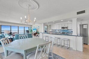 A spacious living area with a large dining table, white chairs, and a view of the ocean. - Luxuriously Remodeled & Expansive Wraparound Ocean Views (Key Colony Beach)