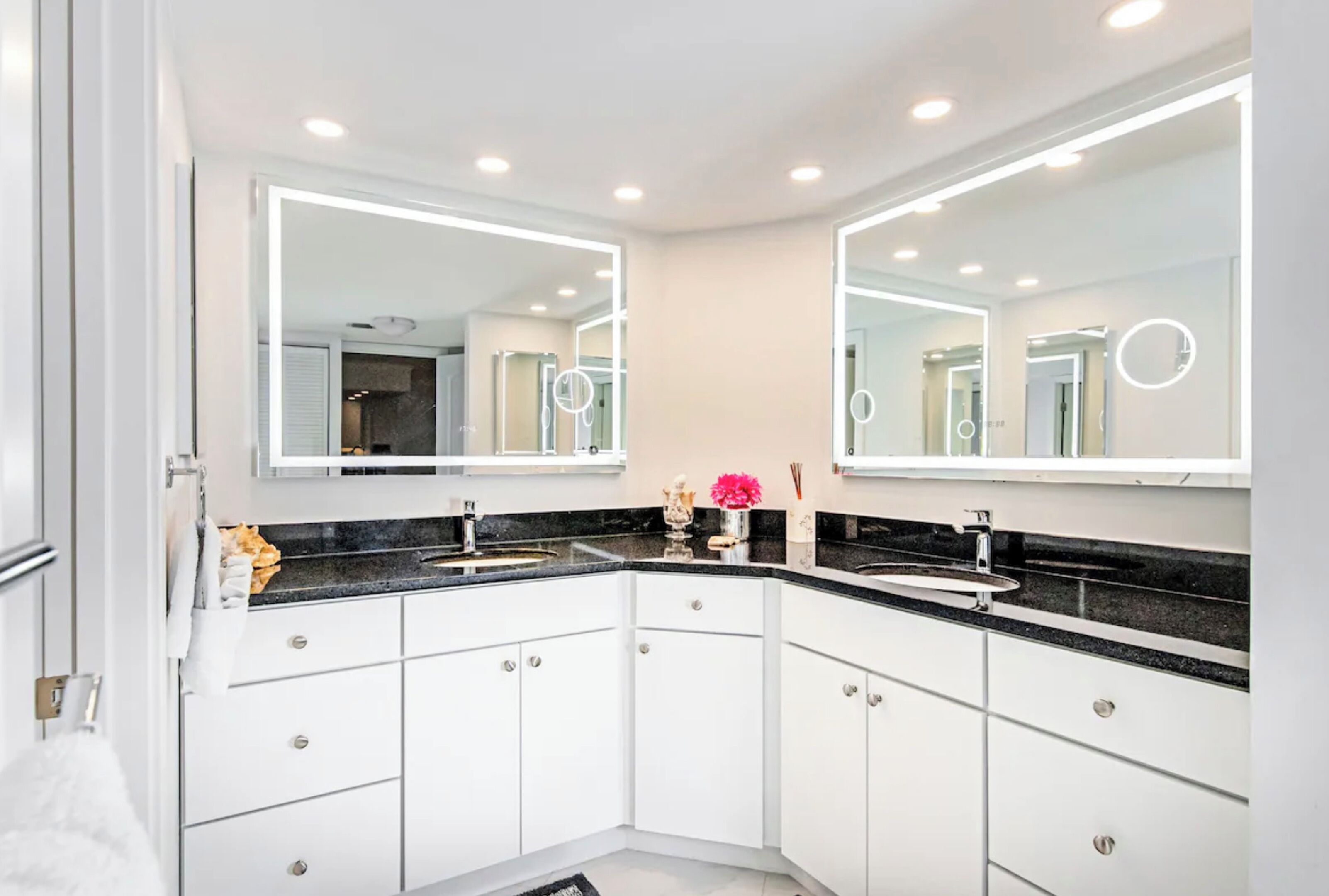 A modern bathroom with two sinks, white cabinets, and a large mirror with built-in lighting.
