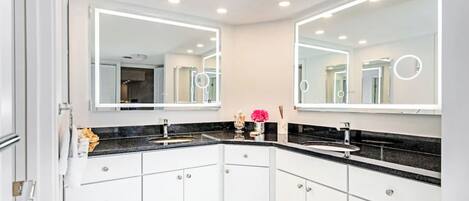 A modern bathroom with two sinks, white cabinets, and a large mirror with built-in lighting.